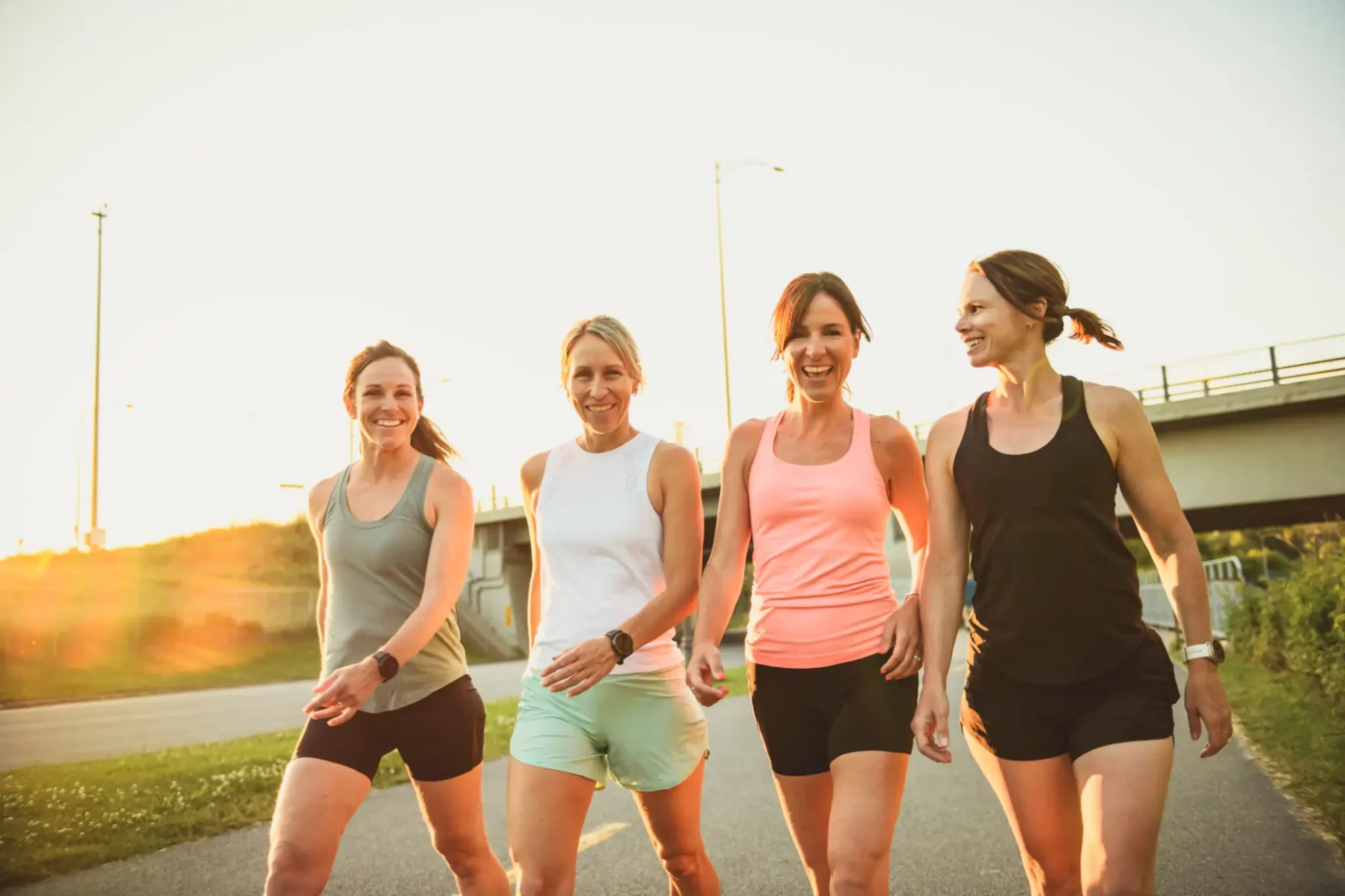 Four women jogging together outdoors at sunset.