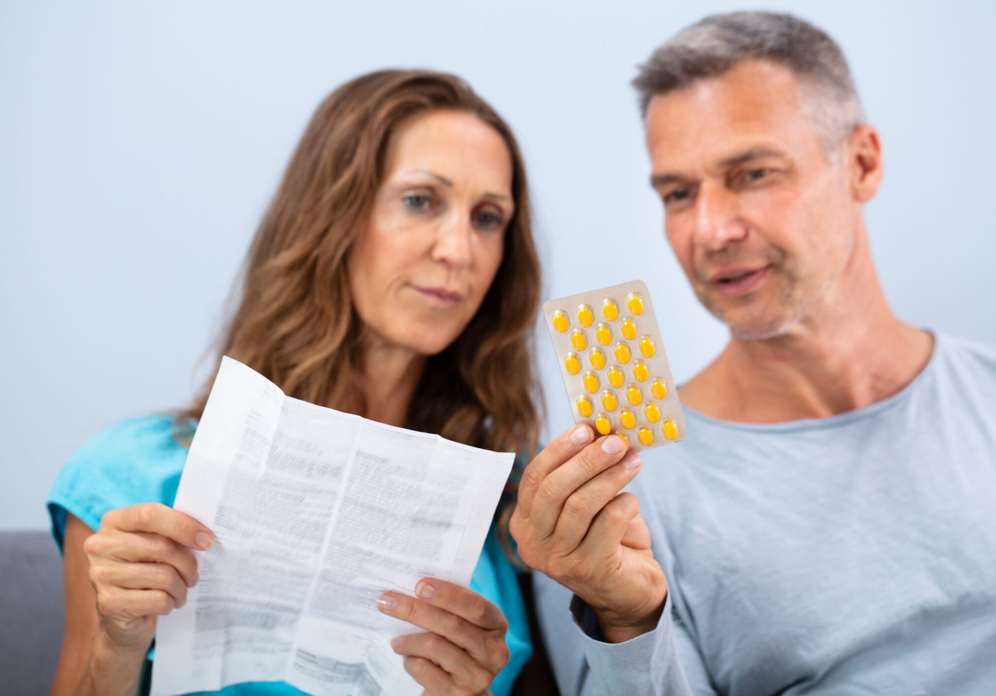 Matured Couple Sitting On Sofa Reading A Leaflet After Taking Pills At Home