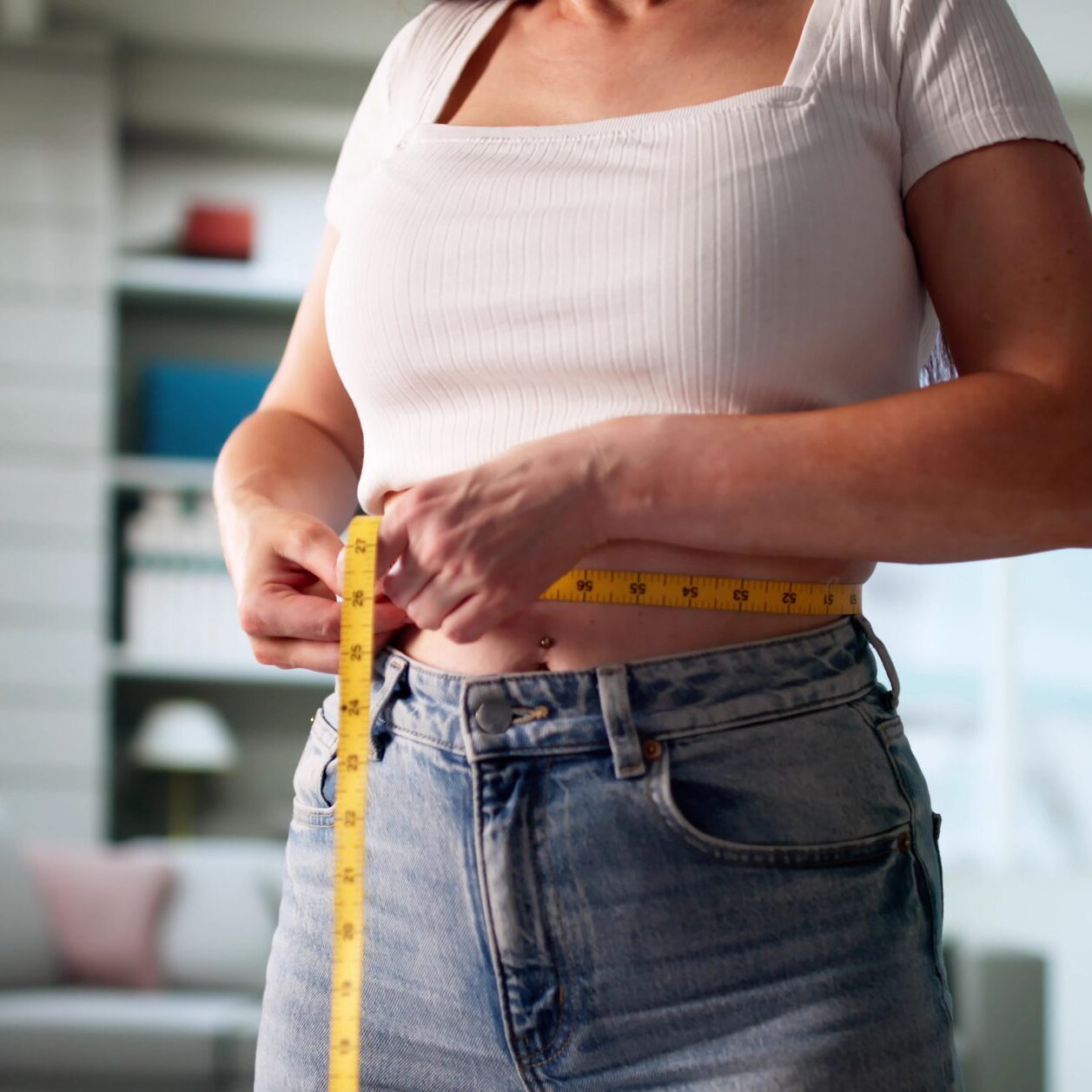 Portrait Of Young Woman Measuring Weight Loss Progress With Tape Measure, Smiling With Satisfaction
